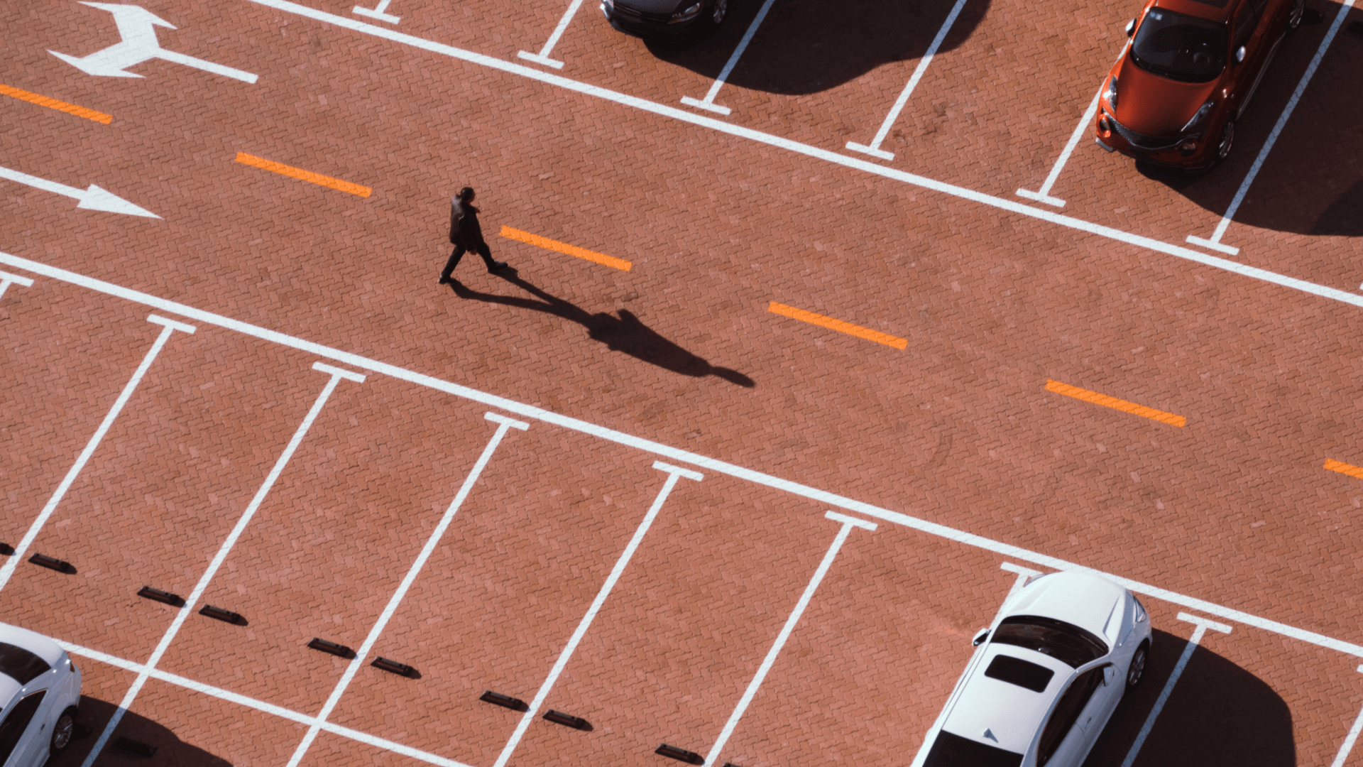 aerial view of a parking lot with a few cars, several empty spaces, and a lone person walking across the road 