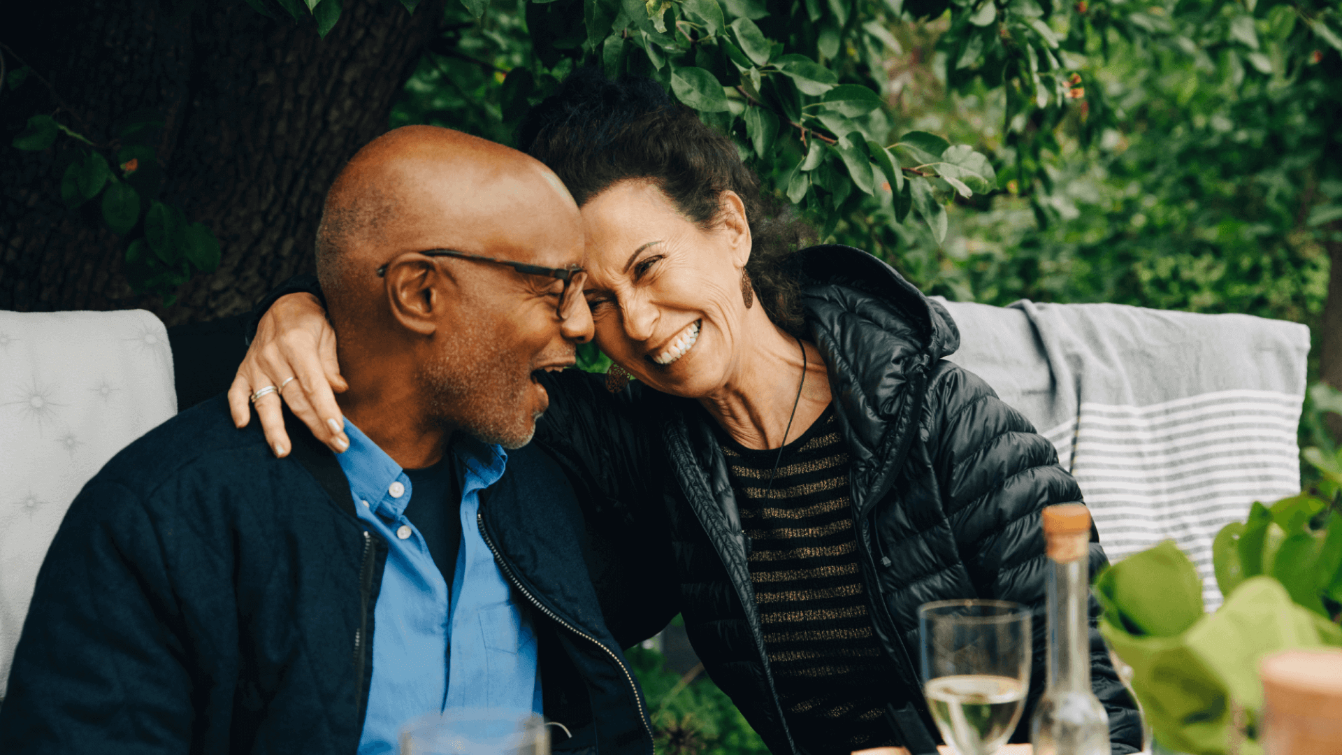 Image featuring a man and a woman sharing a laugh. He's wearing glasses and she has her arm over his shoulder.