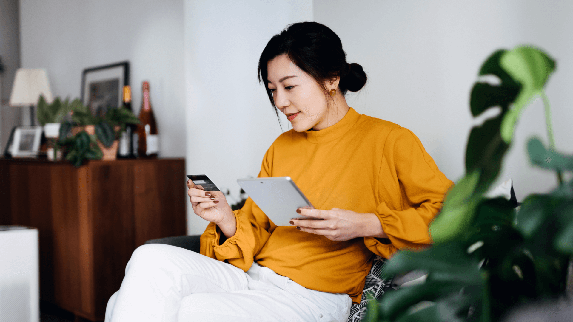 Image featuring a young woman holding a credit card with one hand and a tablet with the other hand.