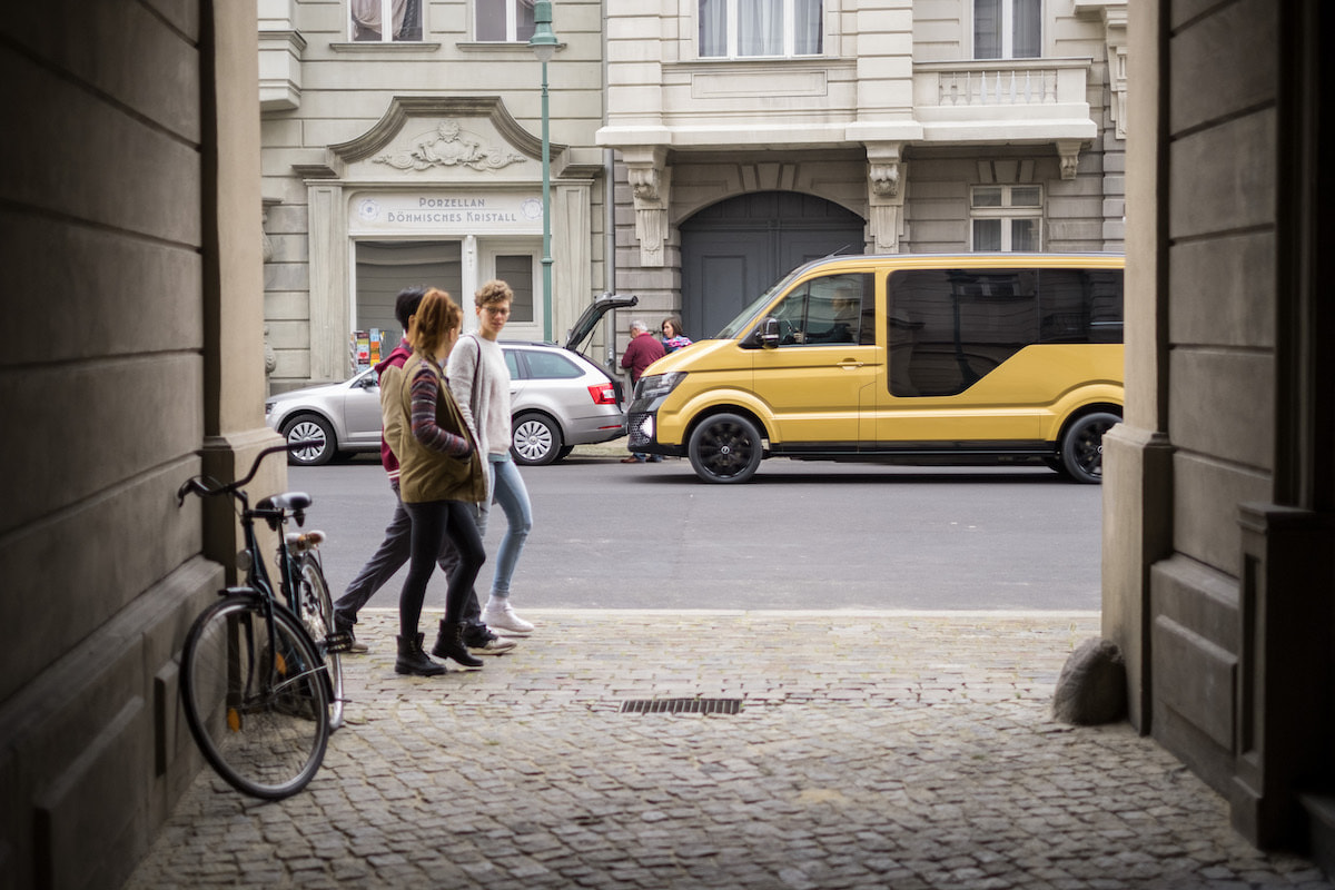 Young caucasian people walking on a street and a driving yellow MOIA truck in the background on the street.