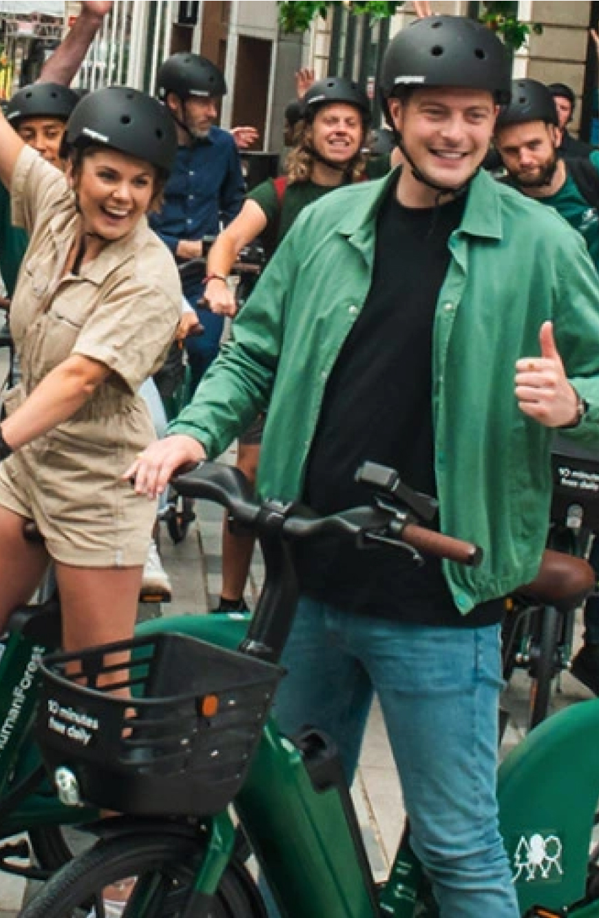 HumanForest customers hero carousel image featuring happy caucasian people standing together wearing helmets while riding ebikes.