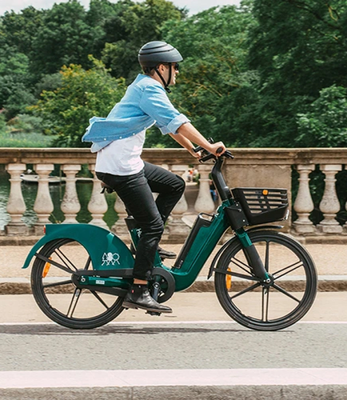 HumanForest customer card image featuring a caucasian man riding an okai e-bike with a helmet on, during a green day in London. 