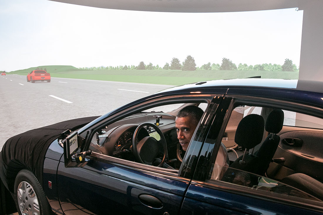 A former African-American president Obama testing out a driving simulator.