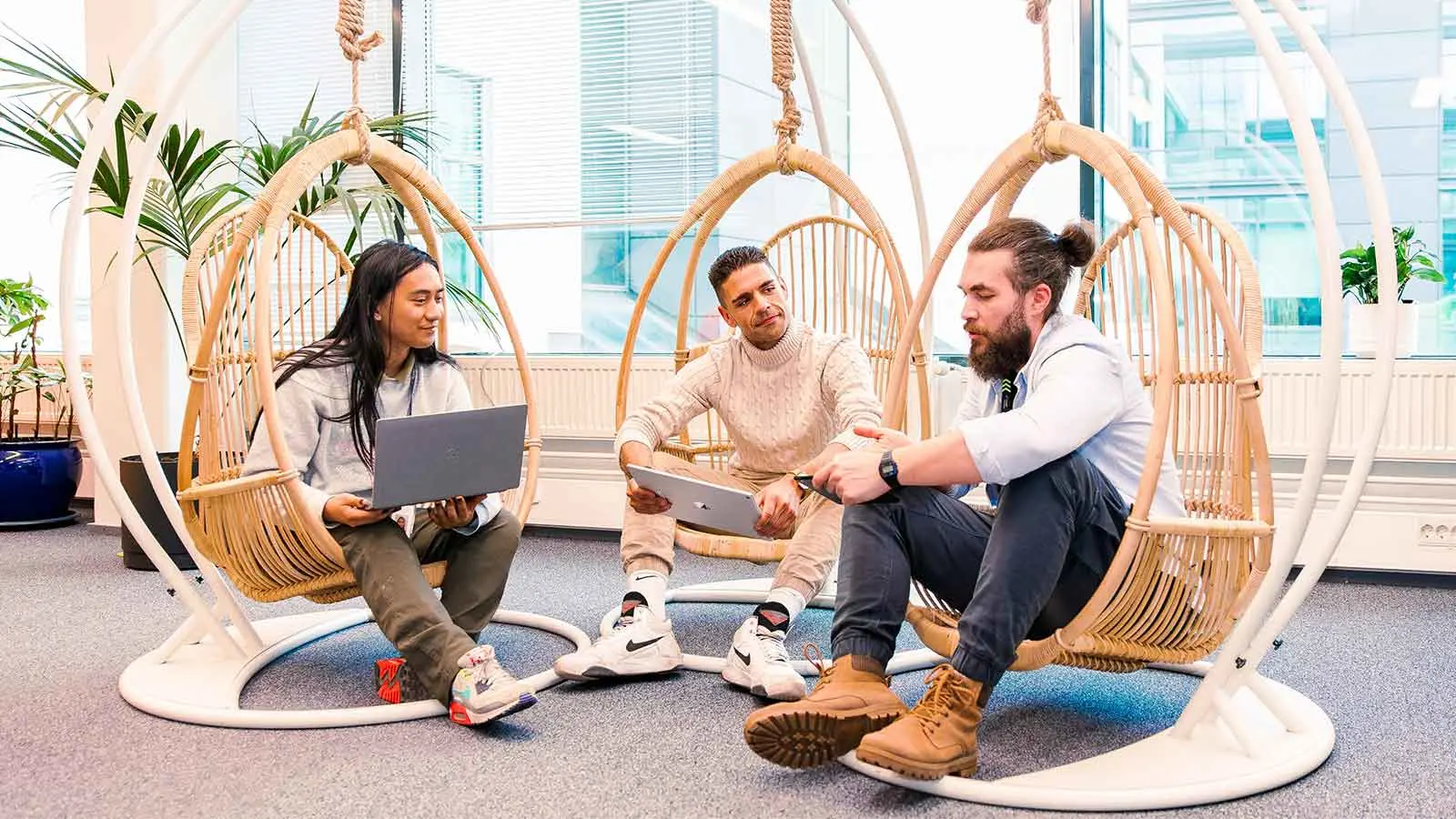 Three co-workers sitting in swing chairs and looking at a laptop. 