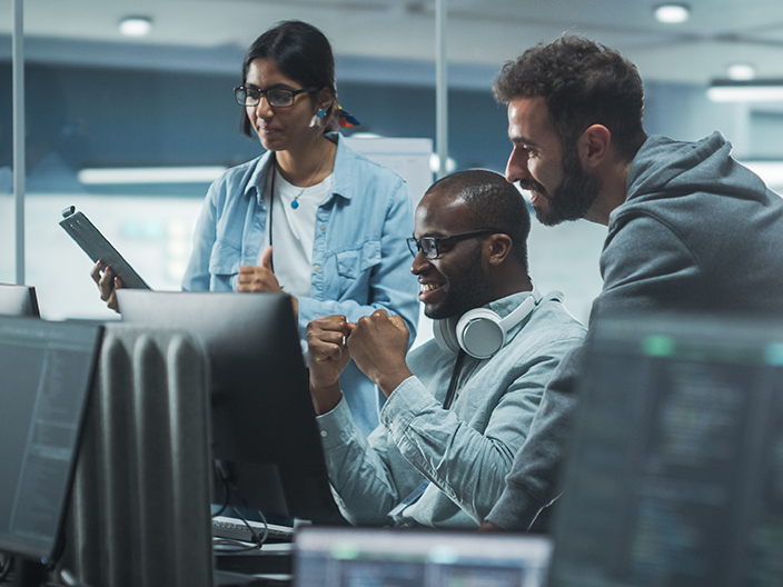 Multiple IT professionals collaborating on a project at a computer.