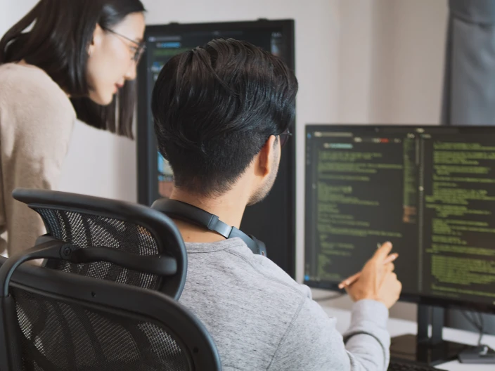 Two people looking at code on a computer.