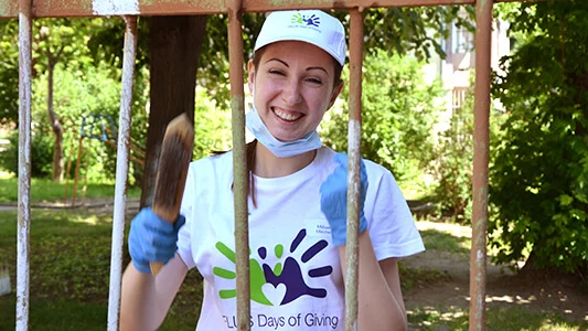 Girl smiling with a paintbrush in front of a fence