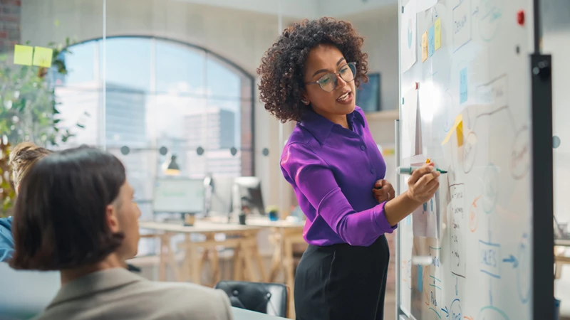 People gathered around a whiteboard in an office setting, with one individual writing on the whiteboard, meant to symbolize the understanding of customer data necessary in customer experience