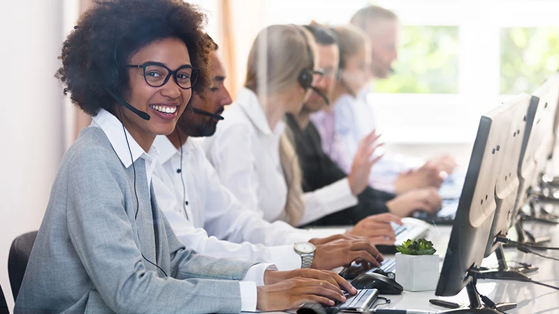 Happy customer support agents sitting at computers and speaking on headsets.