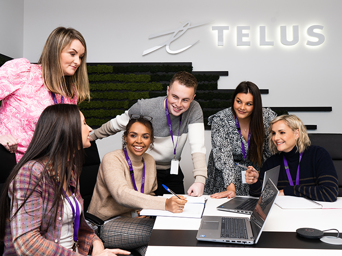 Group of TELUS International team members sitting around a computer