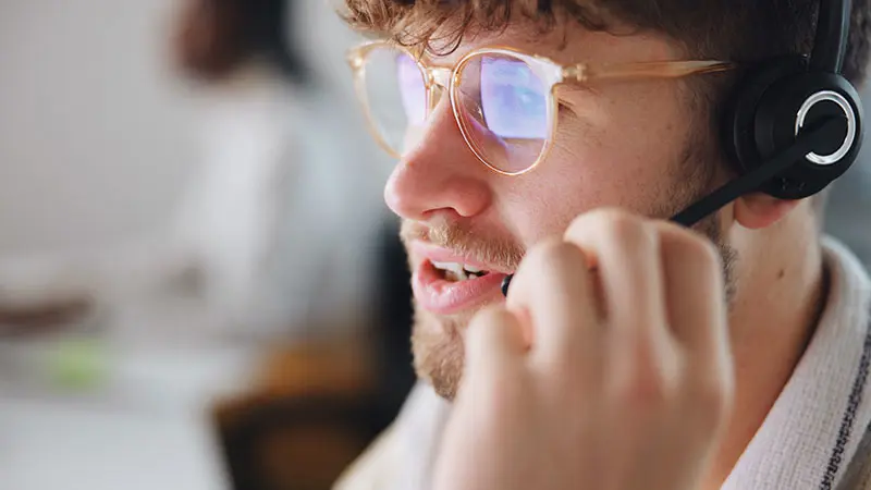 A male customer service agent speaks into a headset. 