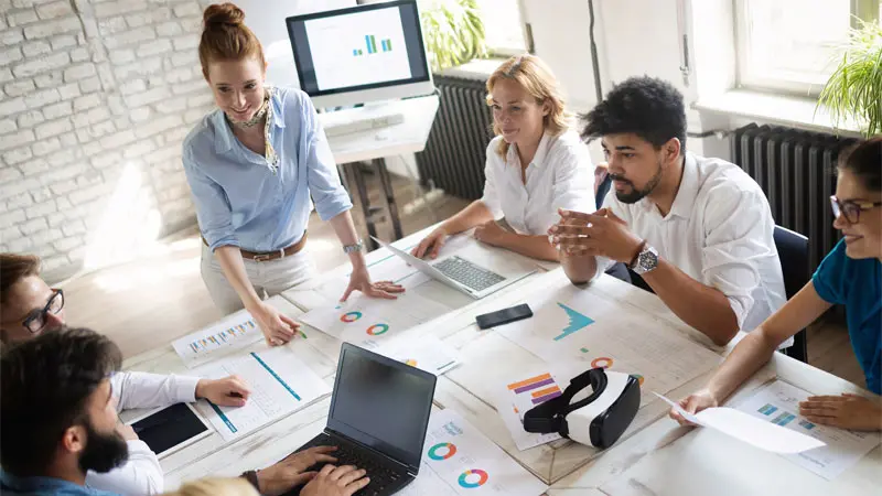 employees meeting around a table with graphs and charts