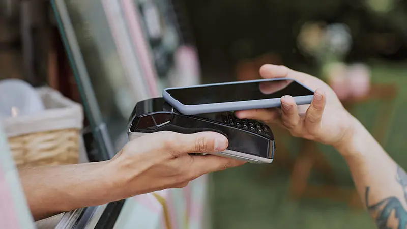Hand holding a mobile device taps it on POS to pay.  
