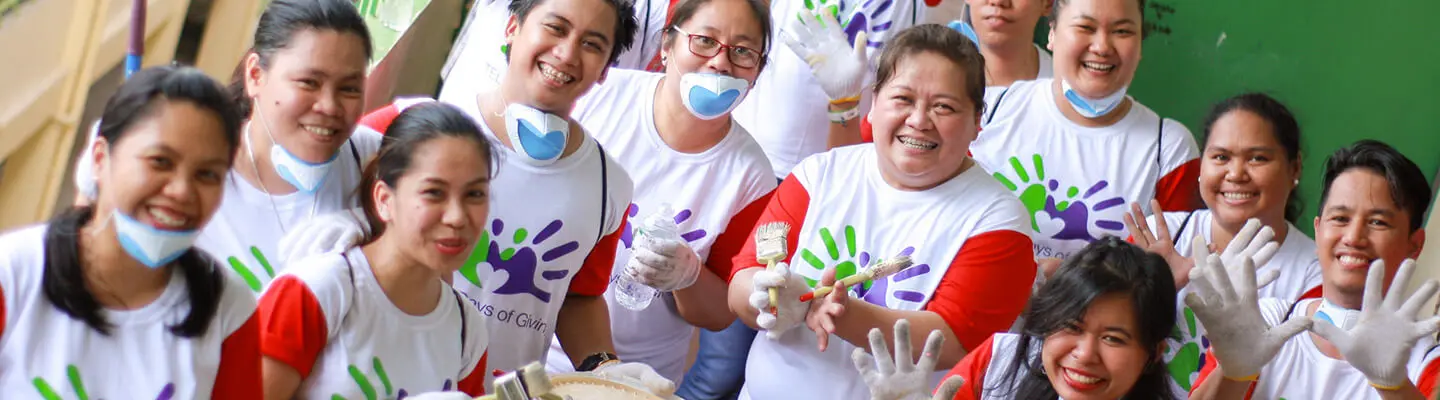 A team of people smiling and holding up their hands while holding paintbrushes