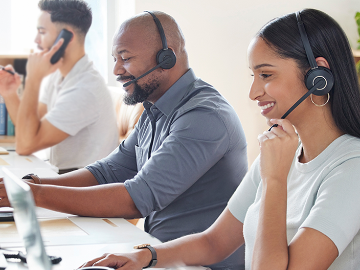 Multiple customer support agents sitting at computers talking to customers on the phone. 