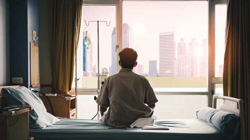 Person sitting on the edge of a hospital bed, looking out to a cityscape and a bright future