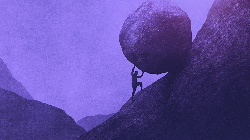 Silhouette of person pushing a boulder up a mountain