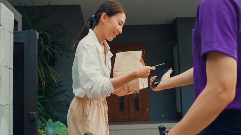 Photograph of customer receiving a food delivery order and using their phone to confirm the transaction