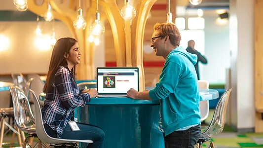 A man and a woman sitting a table with a laptop between them