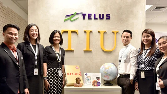 Six people standing in front of a wall that says TELUS TIU and a table with an atlas and a globe
