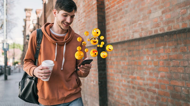 Person walking on street holding coffee and smart phone with emojis floating around it