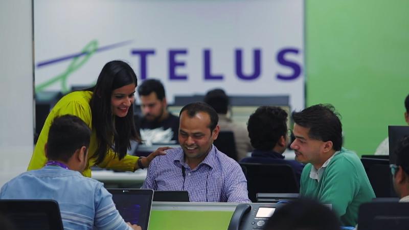 Photograph of team members collaborating with the "TELUS" logo in the background