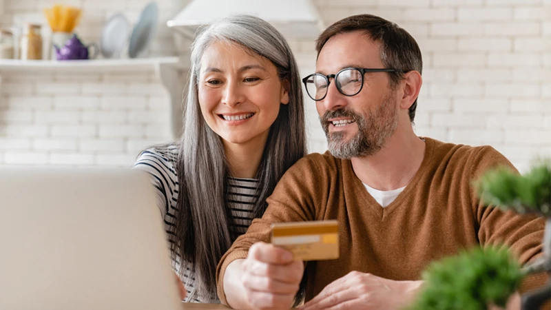 Two people facing a laptop screen and smiling, with one of them holding a credit card