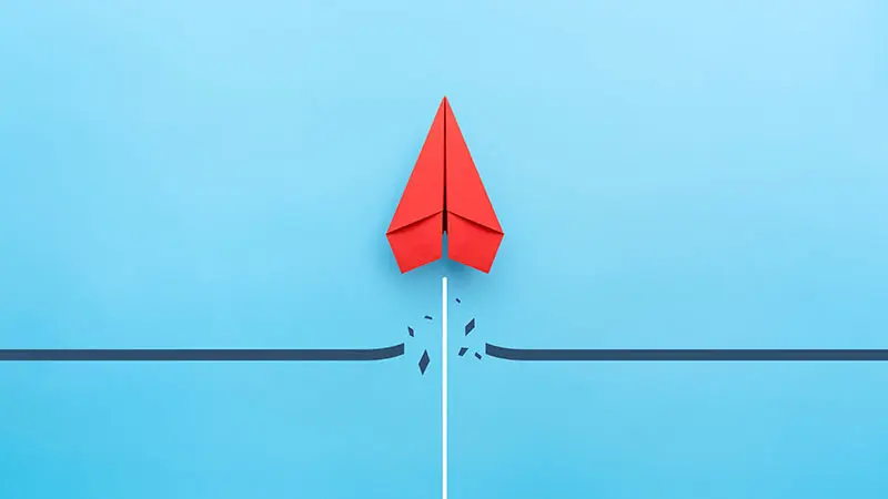 A red paper airplane breaking through an obstacle on a blue background.
