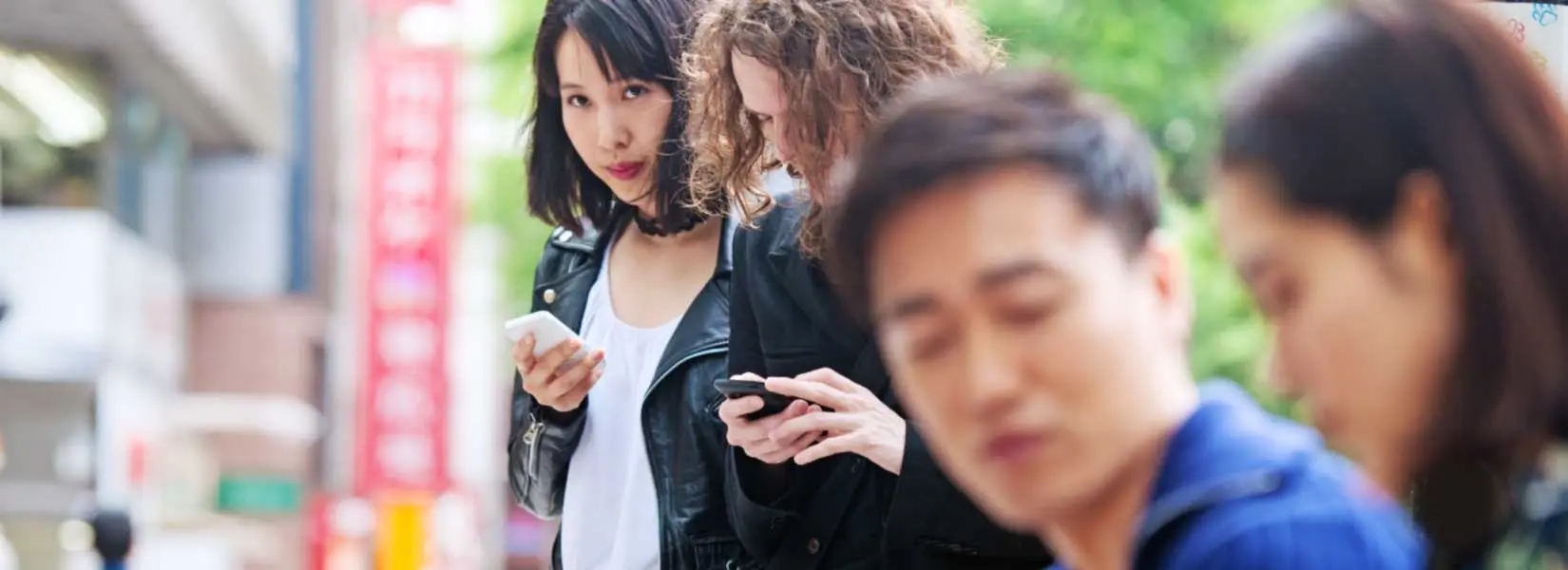 Two individuals on their phones while two blurred people are having a conversation in the foreground