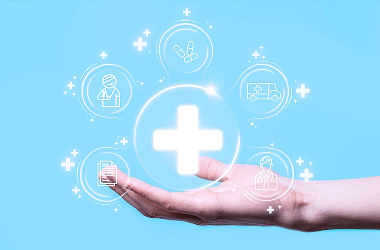 A hand holding illustrations of various icons that represent healthcare, such as, prescription pills, medical documents, an ambulance and a large cross.