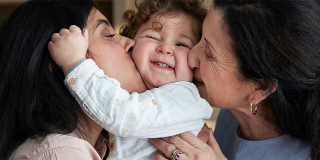 Smiling child being hugged and kissed by two women, one on each side.