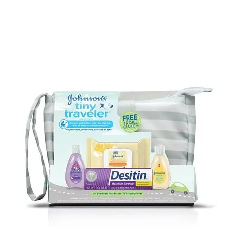 A clear pouch contains baby care products, including lotion, soap, shampoo, and a purple bottle, resting on a white surface. Text: "Johnson's Tiny Traveler Baby Gift Set."