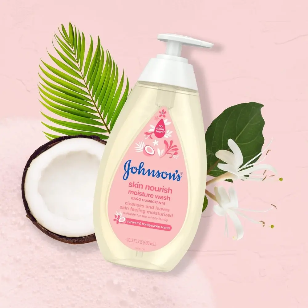 The bottle of Johnson's Skin Nourish Moisture Wash rests on a pink background with a halved coconut, green leaves, and white blossoms. Text: "cleanses and leaves skin feeling moisturized," and more.