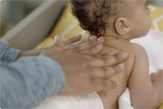 A parent gently massaging their baby's back with both hands, highlighting skincare and tenderness.