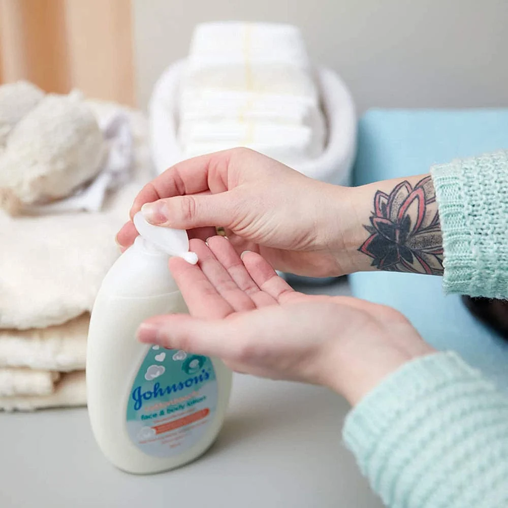 Person dispensing Johnson's Cotton Touch face and body lotion into their hand, with baby care items in the background.