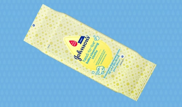 A yellow pack of Johnson's baby wipes lies on a blue patterned surface. Text: "Johnson's baby top-to-toe baby cleansing wipes. Extra moisture. New improved. Gentle from day one. 20 wipes."