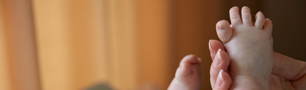 Baby feet gently held by an adult hand, set against a blurred, warm-toned background.