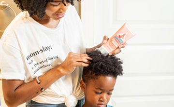 Woman applying hair conditioner to a young child with curly hair in a bathroom setting.