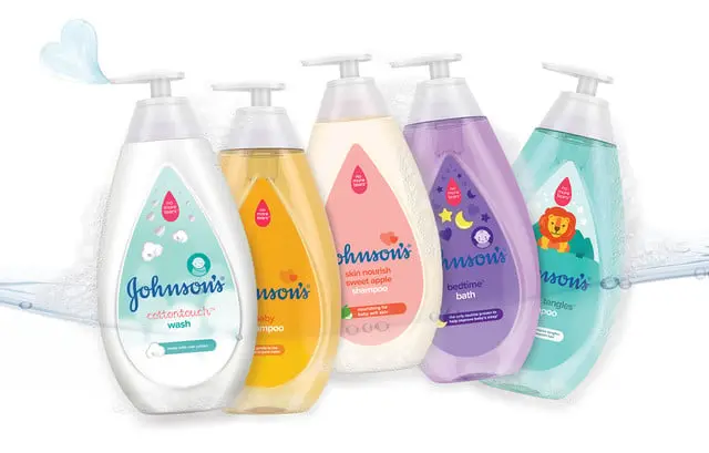 Five bottles of Johnson’s baby products stand upright, each labeled with distinct purposes: cotton touch wash, baby shampoo, sweet apple shampoo, bedtime bath, and no more tangles conditioner.