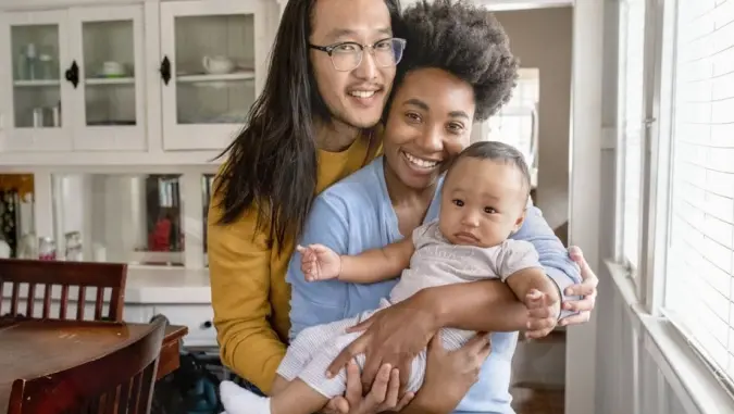 Smiling parents holding their baby in a cozy kitchen setting, showcasing a happy family moment.
