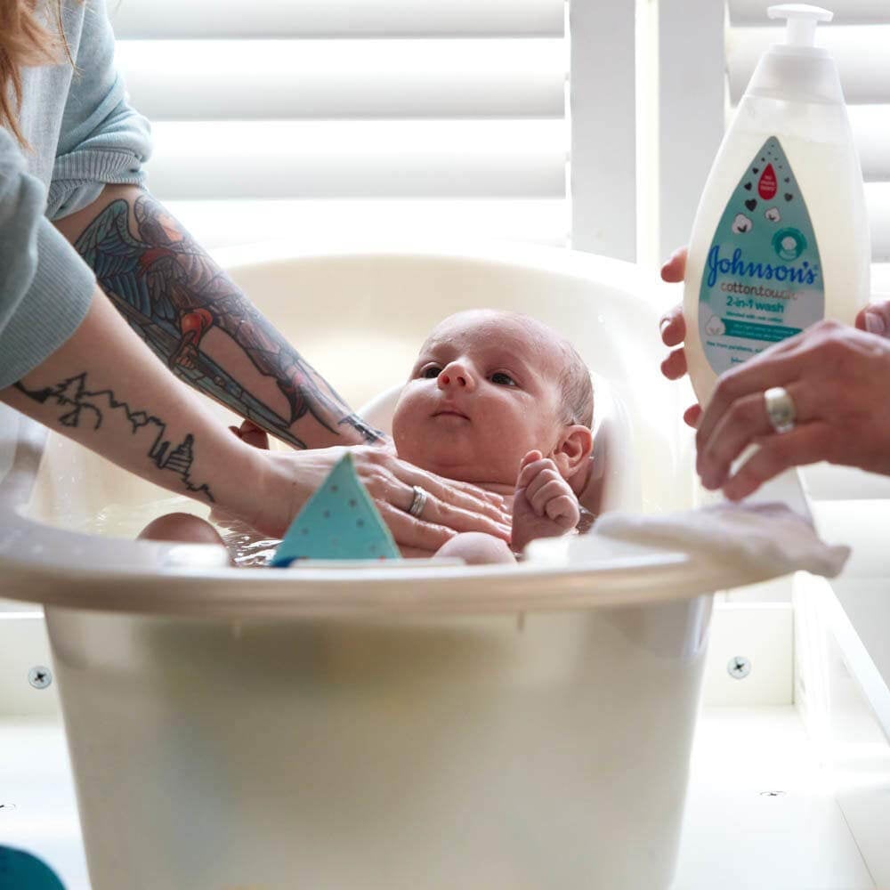 Baby in a bathtub being washed with Johnson's CottonTouch 2-in-1 wash by their parent.