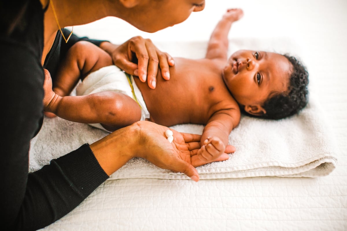 Mother applying lotion to a baby lying on a white towel.