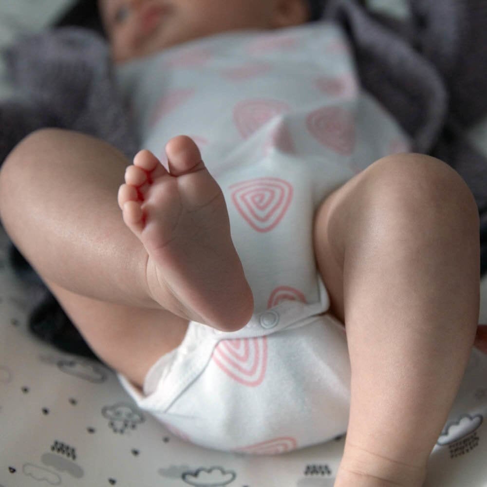 Close-up of baby’s feet wearing a white onesie with pink patterns.