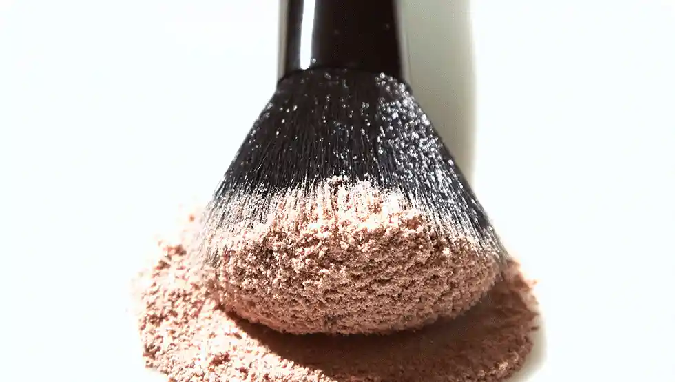 A makeup brush applying loose, light-brown powder, set against a white background.