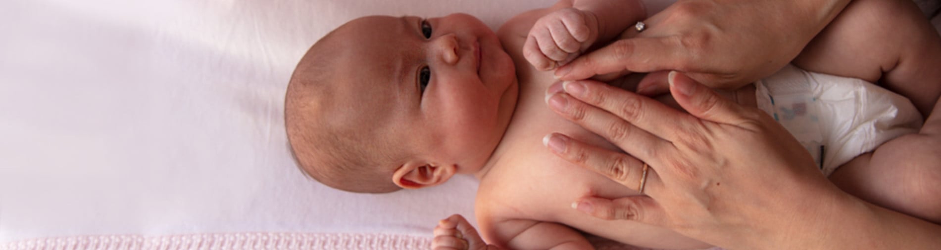 Baby lying on a pink blanket while their parent's hands gently massage the baby's chest.