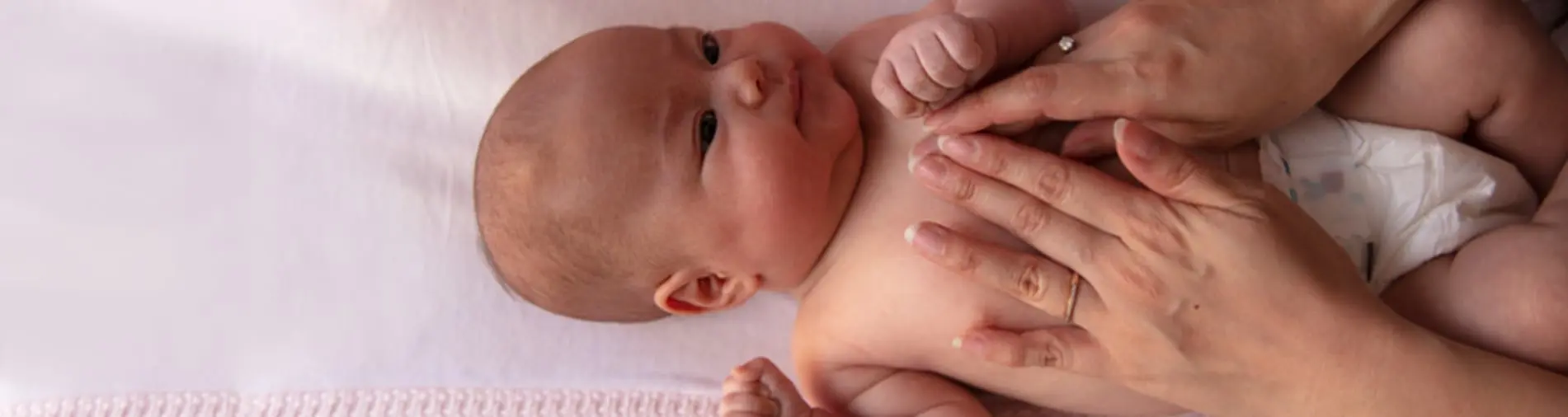 Baby lying on a pink blanket while their parent's hands gently massage the baby's chest.