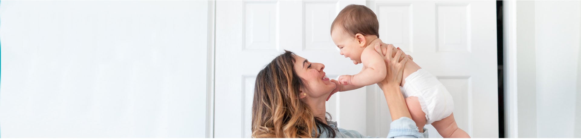 Mother lifting her smiling baby, both looking at each other joyfully.