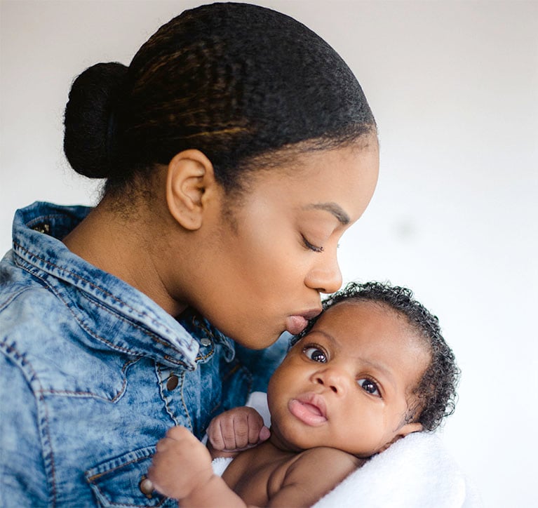 A mother kissing her baby on the forehead while holding them, both sharing a tender moment.