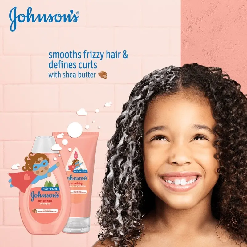 Smiling girl with curly hair covered in lather, next to Johnson's Curl Defining Shampoo and Conditioner bottles with text 'smooths frizzy hair & defines curls with shea butter'.
