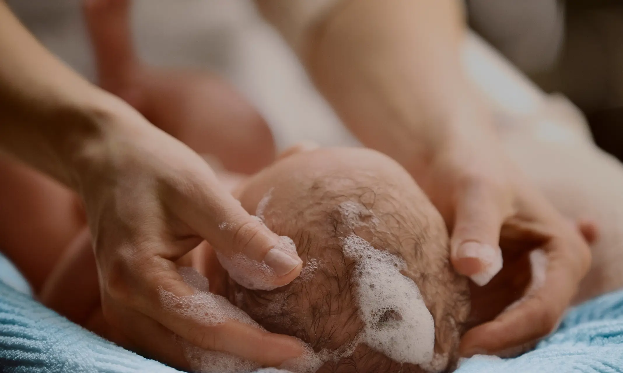 A baby has their hair washed with shampoo, demonstrating a moment of care.